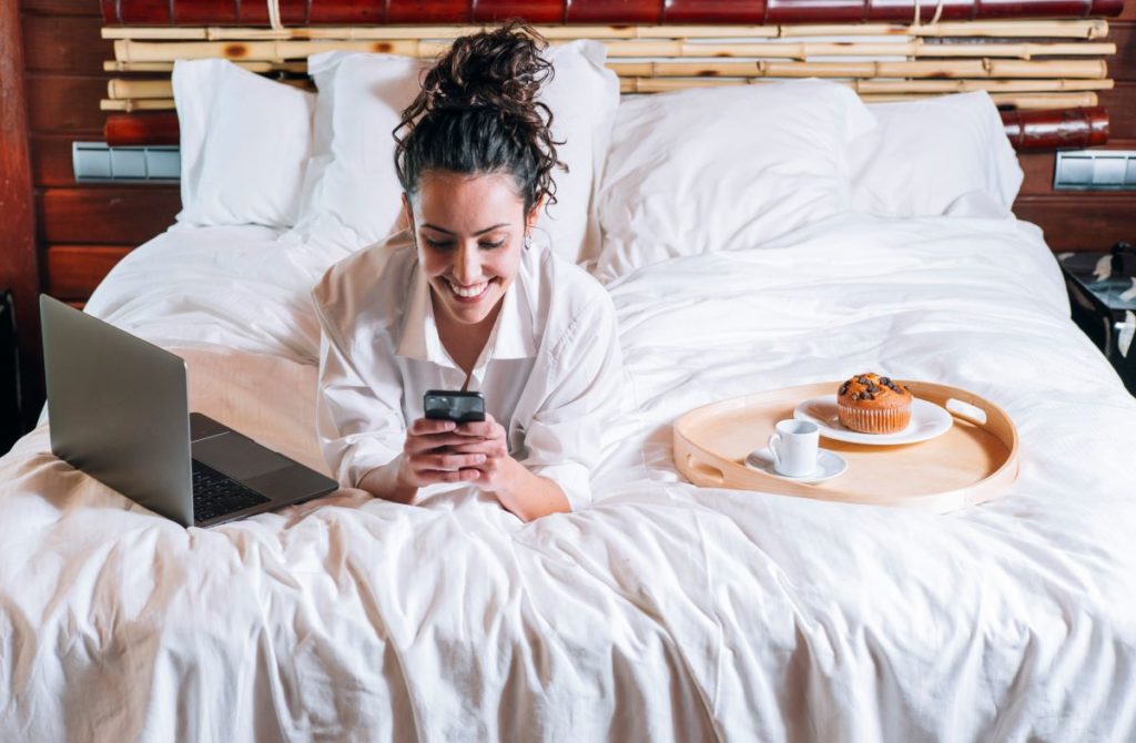 femme avec son téléphone et son ordinateur son sur lit d'hôtel