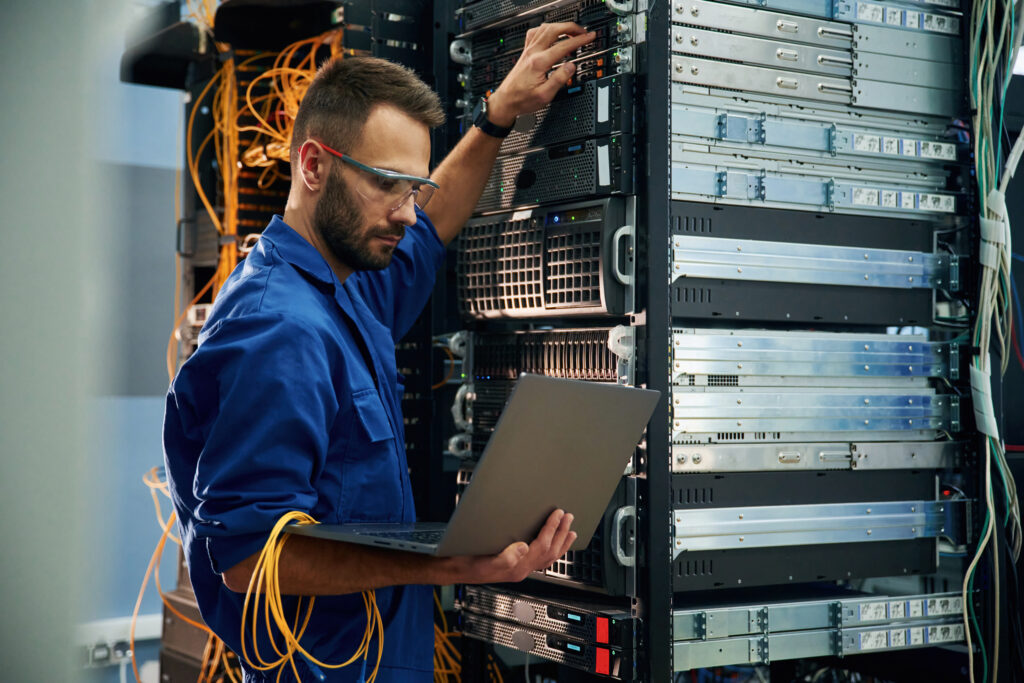 Using the laptop. Young man is working with internet equipment and wires in server room